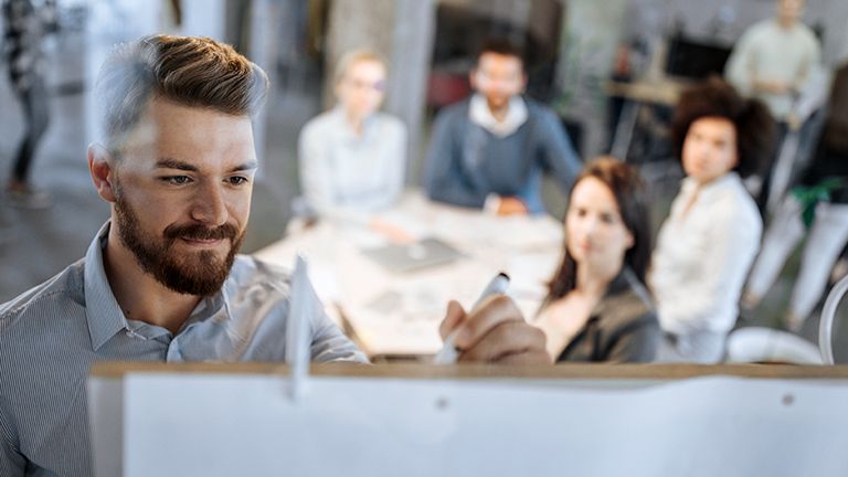 Young businessman writing ideas on whiteboard during a meeting with his colleagues.