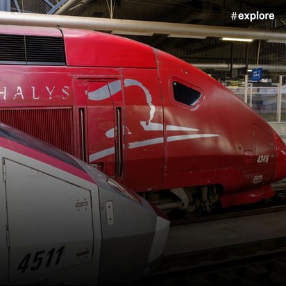 Zwei Züge an einem Bahnhof: Ein roter Zug im Hintergrund und ein grauer-weißer Zug im Vordergrund.