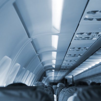 Innenansicht eines Flugzeugkabine mit Sitzreihen und beleuchteten Deckenpaneelen.