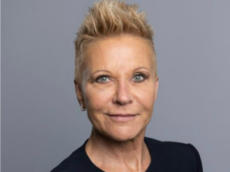 Melanie Vogt mit kurzen, blonden Haaren in einem professionellen Porträt vor grauem Hintergrund.