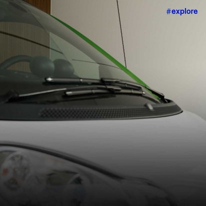 Nahaufnahme eines weißen Elektroautos mit grünen Akzenten links im Bild. Rechts ist durch Glastüren ein moderner Wohnbereich mit Esstisch, gelben Stühlen und einem Fahrrad sichtbar.