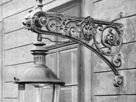 Schwarz-weiß-Fotografie einer dekorativen gusseisernen Wandhalterung für eine historische Straßenlaterne.