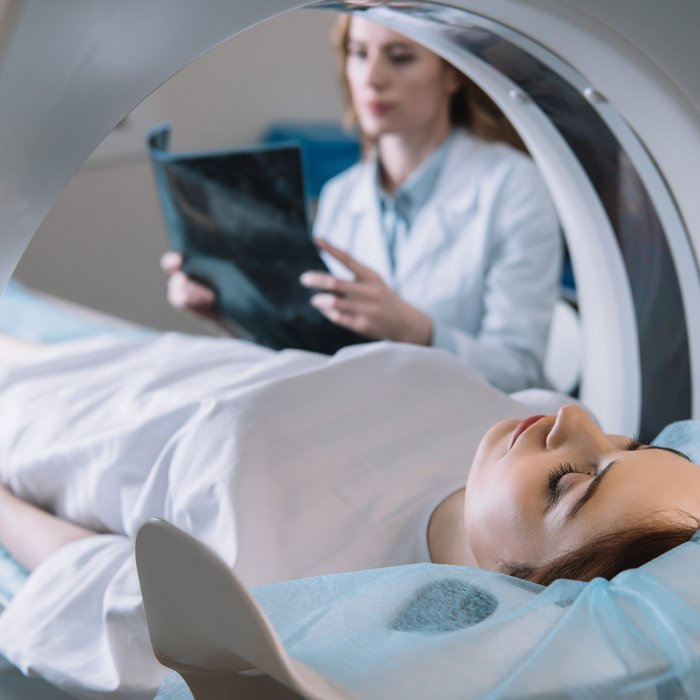 Patientin bei einer CT-Untersuchung mit Röntgentechnik – medizinisches Fachpersonal im Hintergrund