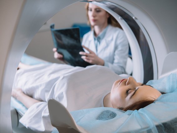 Patientin bei einer CT-Untersuchung mit Röntgentechnik – medizinisches Fachpersonal im Hintergrund