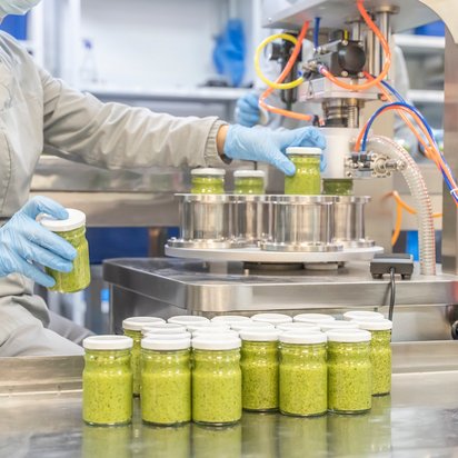 Mitarbeiter befüllt Gläser an einer Abfüllanlage mit einem grünen, cremigen Lebensmittel