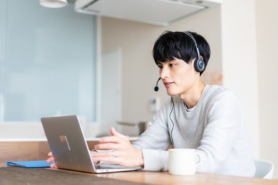 Junger Mann mit Headset nimmt an einem Online-Meeting über Laptop teil.