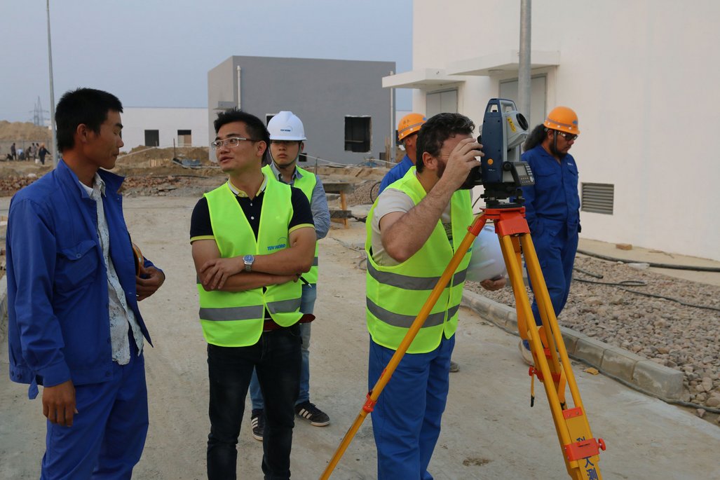 Mehrere Mitarbeiter von TÜV NORD China und Zonergy in Sicherheitswesten stehen draußen und unterhalten sich.