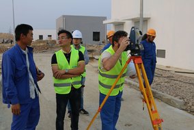 Mehrere Mitarbeiter von TÜV NORD China und Zonergy in Sicherheitswesten stehen draußen und unterhalten sich.