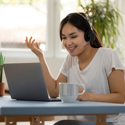 Frau mit Headset sitzt am Laptop und nimmt an einer von der TÜV NORD Akademie organisierten Weiterbildung in englischer Sprache teil.