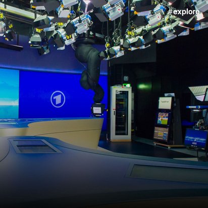 TV-Nachrichtenstudio mit blauem Hintergrund, Moderationstisch, ARD-Logo und zahlreichen Scheinwerfern an der Decke.
