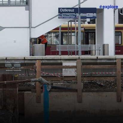 Bahnhof Ostkreuz mit gelb-rotem Zug und sichtbaren Bauarbeiten an den Gleisen.