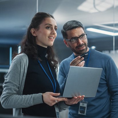 Zwei Personen stehen in einem modernen Büro und betrachten gemeinsam Informationen auf einem Laptop.