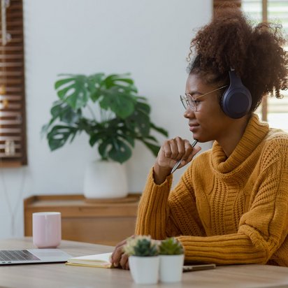 Fokussiertes Arbeiten im Homeoffice während eines Online-Meetings. Frau mit Kopfhörern sitzt am Schreibtisch und nimmt an einem Online-Meeting teil.
