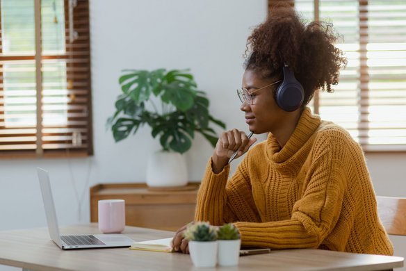 Frau mit Kopfhörern sitzt am Schreibtisch und nimmt an einem Online-Meeting teil.
