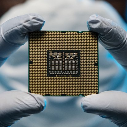 Großaufnahme eines Halbleiters, den eine Person mit Handschuhen zwischen den Zeigefingern und Daumen hält.