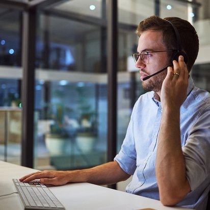 Ein Prüfmittelbeauftragter (TÜV) sitzt in einem Büro am Computer und telefoniert mit einem Headset