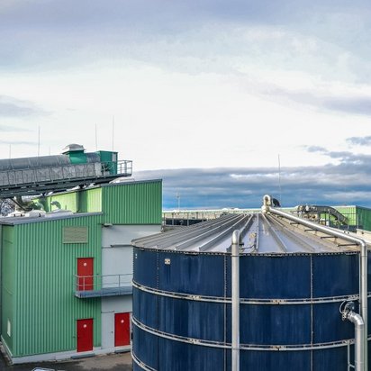 Industrielle Anlage mit grünen Gebäuden, großen Fermentern und Rohrleitungen, vermutlich Teil einer Biogas- oder Energieerzeugungsanlage.