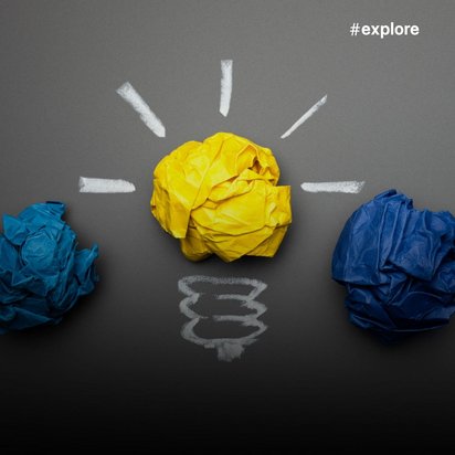 Zwei zerknüllte Papierbälle in verschiedenen Blautönen liegen in einer Reihe, wobei der mittlere gelbe Ball als leuchtende Glühbirne dargestellt ist.