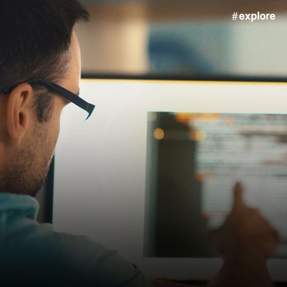 Eine Person mit Brille und türkisfarbenem Oberteil betrachtet einen Computerbildschirm mit Programmcode.