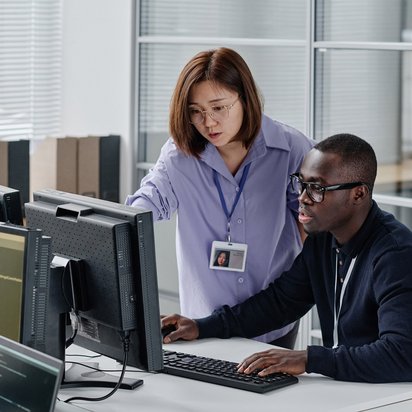 Zwei IT-Fachkräfte arbeiten gemeinsam an Code auf mehreren Monitoren in einem modernen Büro