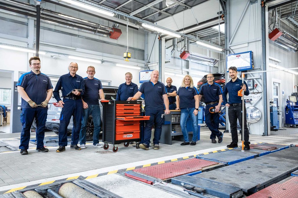 TÜV NORD Werkstatt-Team in Arbeitskleidung steht gemeinsam in der Prüfhalle, umgeben von Werkstattausrüstung.