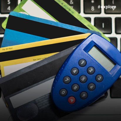 Ein blauer elektronischer TAN-Generator mit Display und Tastatur liegt auf einer Laptop-Tastatur, daneben befinden sich mehrere bunte Bankkarten in verschiedenen Farben (blau, gelb, grau, grün). Das Bild zeigt typische Online-Banking-Utensilien für sichere Transaktionen und digitale Zahlungen.