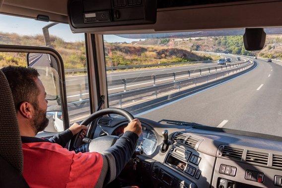Mann in rotem Shirt steuert einen Lkw auf einer kurvigen Autobahn