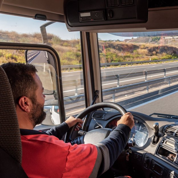 Mann in rotem Shirt steuert einen Lkw auf einer kurvigen Autobahn