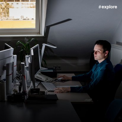 Ein Computerforensiker oder IT-Sicherheitsexperte arbeitet konzentriert an mehreren Bildschirmen in einem abgedunkelten Dachbüro.