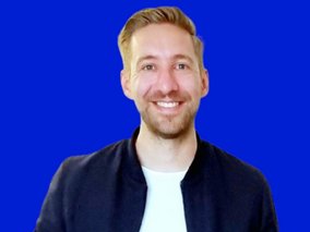 Thomas Hoger mit blondem Haar vor einem kobaltblauen Hintergrund, trägt eine dunkle Jacke.