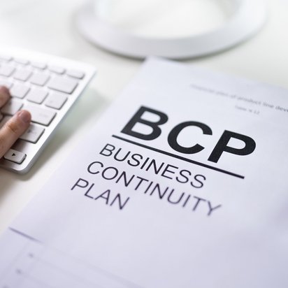 Hand auf Tastatur neben einem Dokument mit der Aufschrift "BCP Business Continuity Plan".