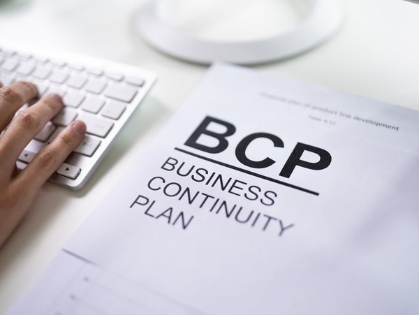  Hand auf Tastatur neben einem Dokument mit der Aufschrift "BCP Business Continuity Plan".