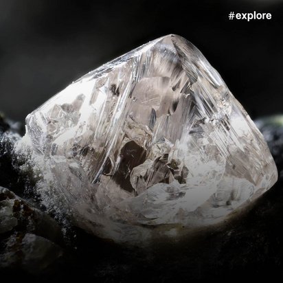 Großer durchsichtiger Kristall oder Diamant liegt auf dunklem, rauem Gestein in dramatischer Beleuchtung.