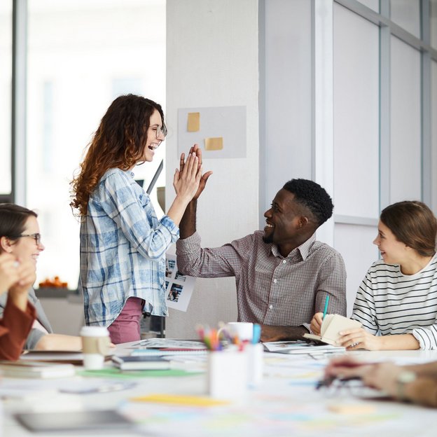 Team feiert gemeinsamen Erfolg mit High Five in kreativem Arbeitsumfeld