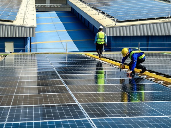 Zwei Arbeiter installieren oder warten Photovoltaikmodule auf einem Flachdach.