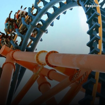 Spektakuläre Achterbahn mit blau-gelben Schienen und orangefarbener Stützkonstruktion in leicht nebligem Himmel.