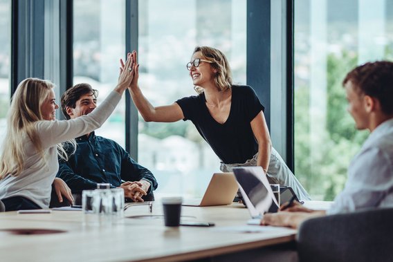 Zwei Kolleginnen geben sich ein High-Five während eines Meetings in einem modernen Konferenzraum.