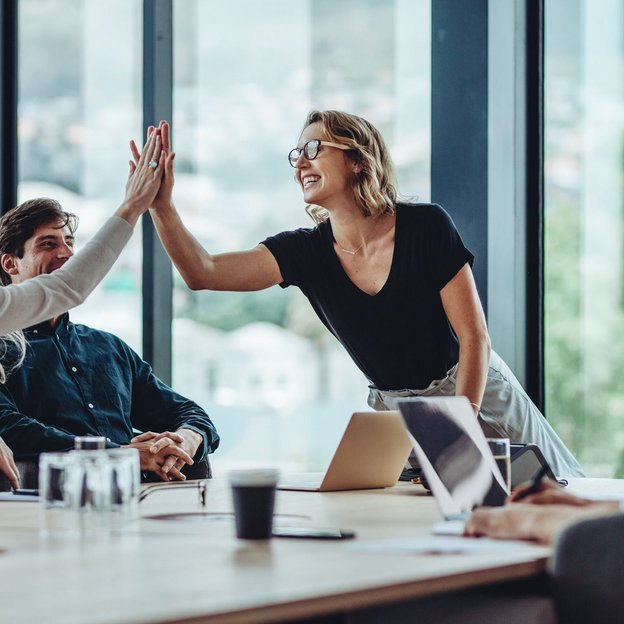 Zwei Kolleginnen geben sich ein High-Five während eines Meetings in einem modernen Konferenzraum.