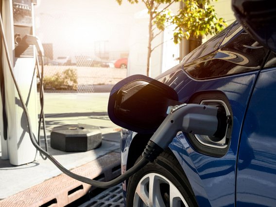 Ein blaues Elektroauto wird an einer weißen Ladestation aufgeladen, das schwarze Ladekabel ist in den Ladeanschluss am Fahrzeug eingesteckt.
