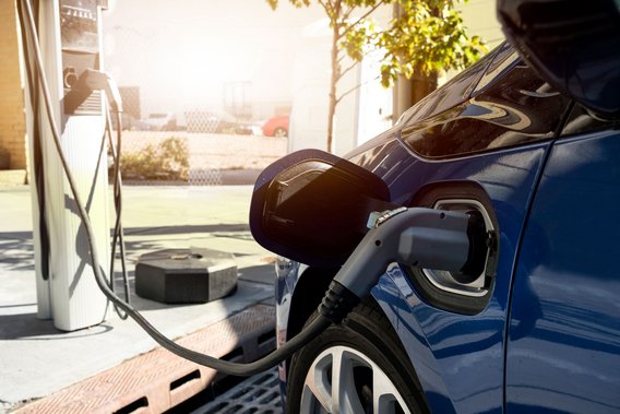 Ein blaues Elektroauto wird an einer weißen Ladestation aufgeladen, das schwarze Ladekabel ist in den Ladeanschluss am Fahrzeug eingesteckt.