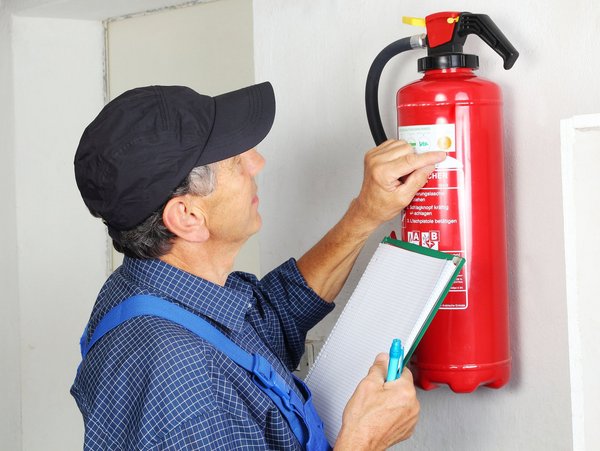 Mann mit Kappe prüft einen Feuerlöscher und notiert sich Details auf einem Klemmbrett.