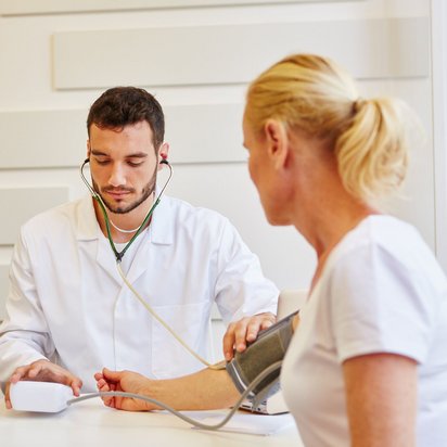 Ein Arzt misst den Blutdruck einer Patientin während einer arbeitsmedizinischen Untersuchung.
