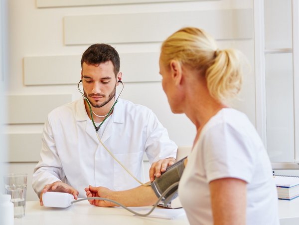 Ein Arzt misst den Blutdruck einer Patientin während einer arbeitsmedizinischen Untersuchung.