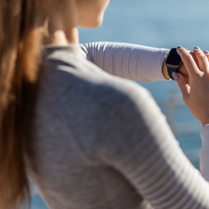 Frau prüft ihre Smartwatch im Freien mit Blick auf das Wasser im Hintergrund.