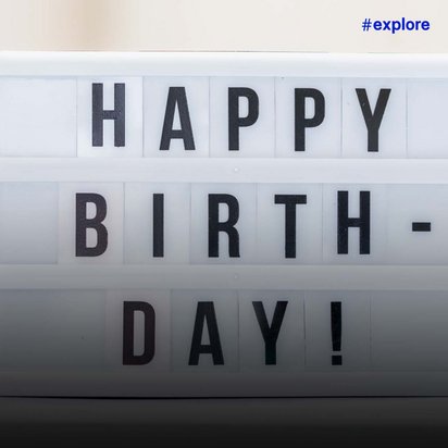 Ein beleuchtetes weißes Schild mit schwarzen Großbuchstaben zeigt die Aufschrift "HAPPY BIRTH-DAY!" auf einem weichen, unscharfen Hintergrund.