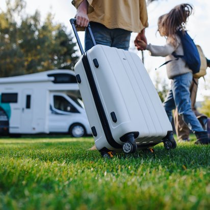 Familienreise mit Wohnmobil und Gepäck auf der Wiese Familie mit Gepäck vor einem Wohnmobil auf einer Wiese