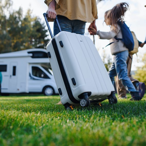 Familie mit Gepäck vor einem Wohnmobil auf einer Wiese