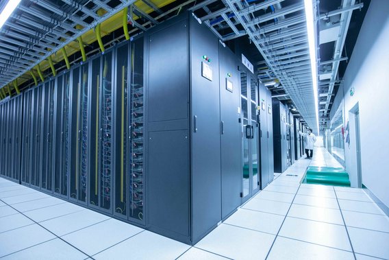 Blick in einen modernen Serverraum mit langen Reihen von Server-Racks und einem Techniker, der die Systeme überprüft.