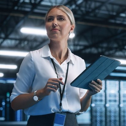 Security Incident Manager (TÜV) Ein Security Incident Manager steht in einem Rechenzentrum und hält ein Tablet, während sie Daten oder Systeme überprüft.