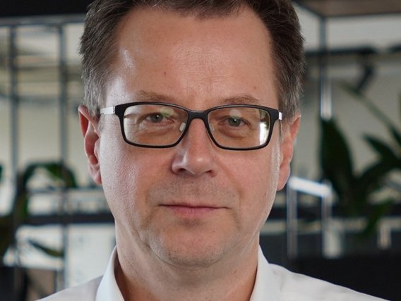 Thomas Kattenstein mit kurzen braunen Haaren und schwarzer Brille in einem weißen Hemd, der direkt in die Kamera blickt.